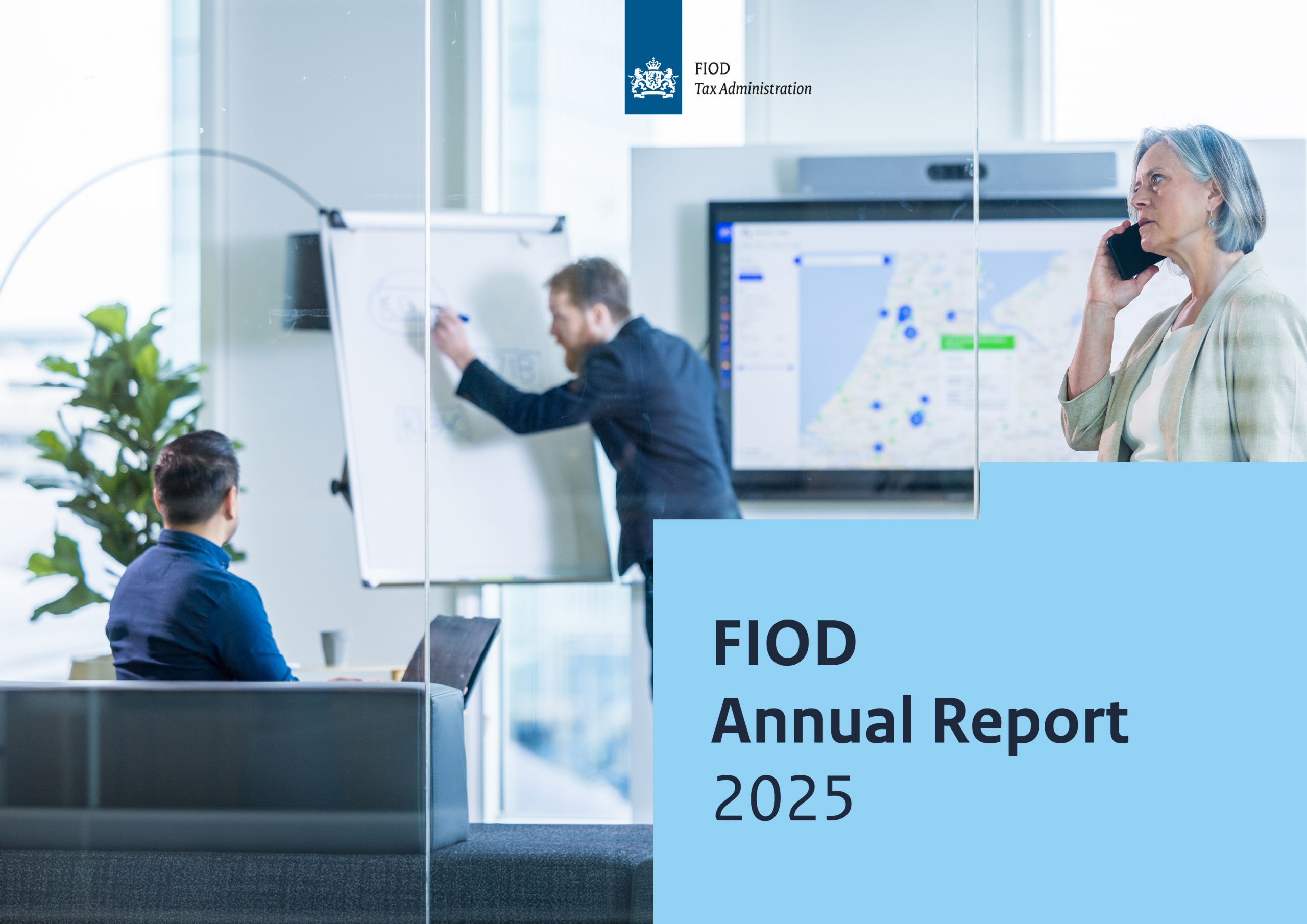 Front cover of the FIOD Annual Report 2025: a white office with dark furniture, set against a screen displaying a world map and statistics. In the background, two men are discussing information, while a woman in the foreground is talking on the phone. In the bottom right corner, a blue block shows the text “FIOD Annual Report 2025.”