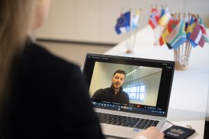 Foto van vrouw achter laptop met persoon op scherm.