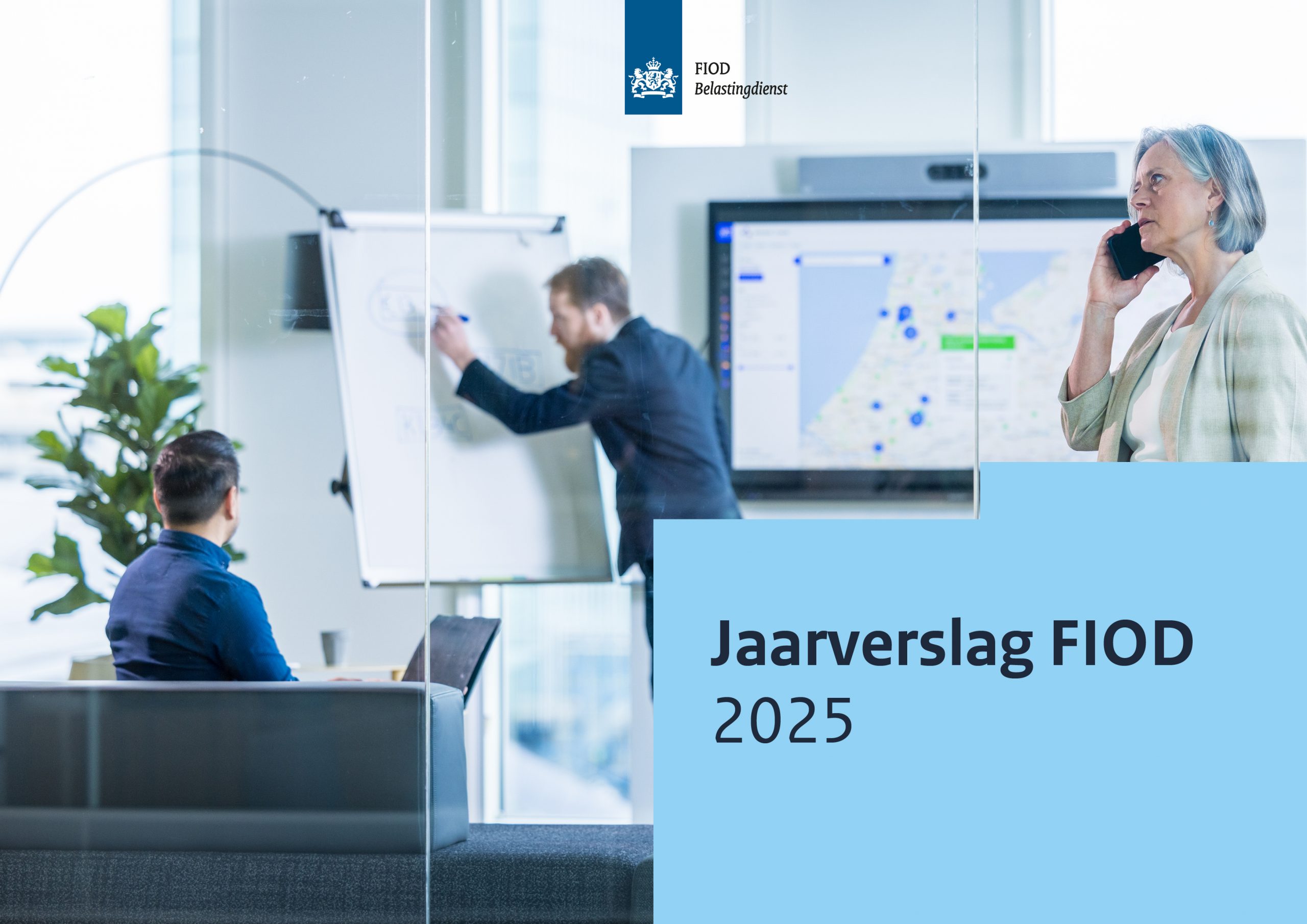 De voorkant van het jaarverslag FIOD 2025 is een foto van een wit kantoor met donkere meubels, tegen een achtergrond van een scherm met daarop een wereldkaart en statistieken. 2 mannen bespreken informatie met elkaar op de achtergrond. Op de voorgrond staat een vrouw te telefoneren. Rechtsonder is een blauw blok met daarin de tekst: Jaarverslag FIOD 2025